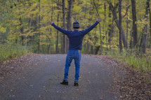 a man standing on a country road with arms raised 