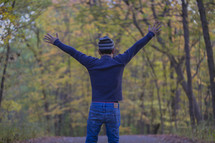 a man standing in the middle of a country road with arms raised 