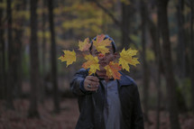 man holding a branch full of fall leaves in front of his face 