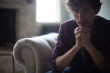 a man sitting on a couch in prayer 