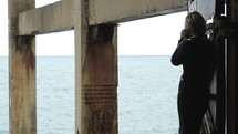 Woman underneath a pier looking out at the ocean.