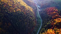 Aerial view of a rural valley surrounded by autumn forests, a road in a valley, a foothill village in the glow of sunlight. 