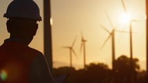 Silhouette of a man Engineer against wind power plant generator at sunset