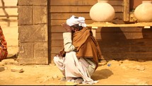 a man sitting covering his eyes from the sun in a desert village