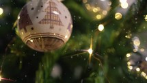 White ball hanging from a Christmas tree with snow falling 