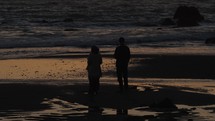 Tilt up of couple watching sun set as waves crash on rocks