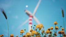 Blurred Wind power plant turbine for electric clean energy near a park of flowers at sunset