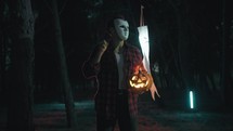 Masked man with axe and halloween pumpkin walk in the forest