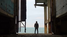 Man standing underneath a pier looking out at the ocean.