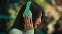 Young female model listening to music with modern headphone in park with blurred background 