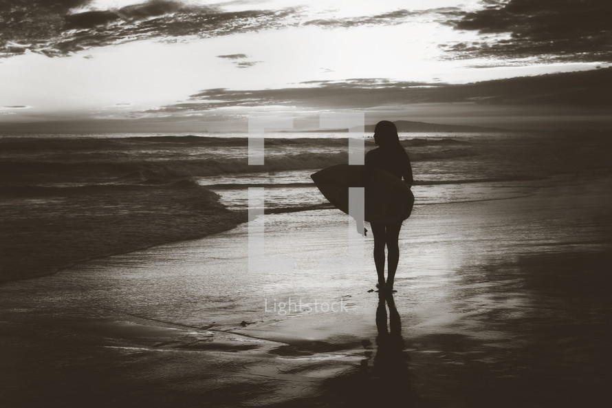 a silhouette of a female surfer standing on a beach 