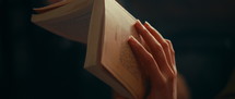 Girl's hand is holding a book and flipping through the book
