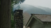 Smoke comes out of cabin chimney with with snow covered hills in the background