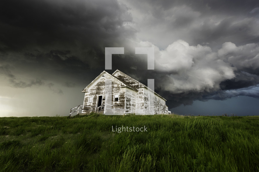 Old School House Sits Under A Menacing Storm Cloud With Lush Green Grass