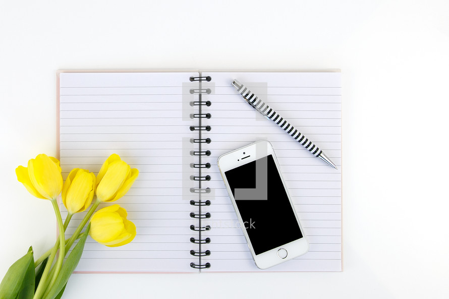 yellow tulips, open notebook, blank pages, cellphone, and pen 