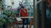 Female owner of plant shop standing in room decorated with green houseplants, talking with customer on the phone and using laptop while taking order from online store
