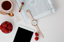 Raspberries in a bowl, watch, magazine, rings, tablet, lipstick, spoon, and coffee cup