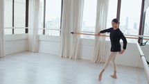 Young beautiful ballerina dancing gracefully in a spacious studio during rehearsal at daytime, performing classical ballet steps and turns. Full length shot
