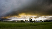 Storm Clouds are Turned Beautiful Colors at Sunset Above a Small Farm.