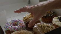 Womans hand grabs a sprinkle donut from a box of 6 fresh delicious donuts