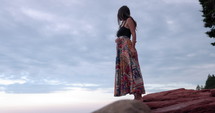 Young hippy woman meditating by ocean on blue cloudy sky - wide shot
