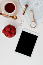 Raspberries in a bowl, watch, lipstick, tablet, magazine, rings, spoon, and coffee cup