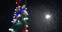 Slow motion snow at night falling in city with Christmas lights, Snowflakes falling in slow motion during winter snow storm at nighttime.