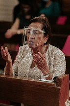 elderly woman in a face shield praying in church 