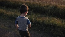 Young happy boy playing outside throwing dirt in slow motion in sunlight during sunset.