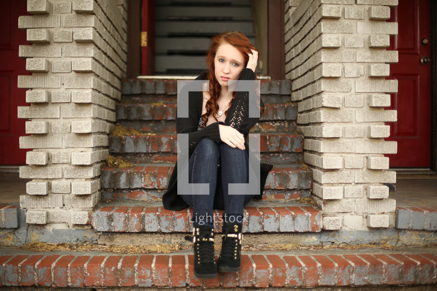 a confused teen girl sitting on brick stairs 