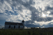 Country church under stormy sky with sunburst through dark clouds