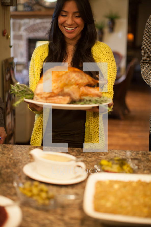 woman carrying a Thanksgiving turkey to a dinner table 
