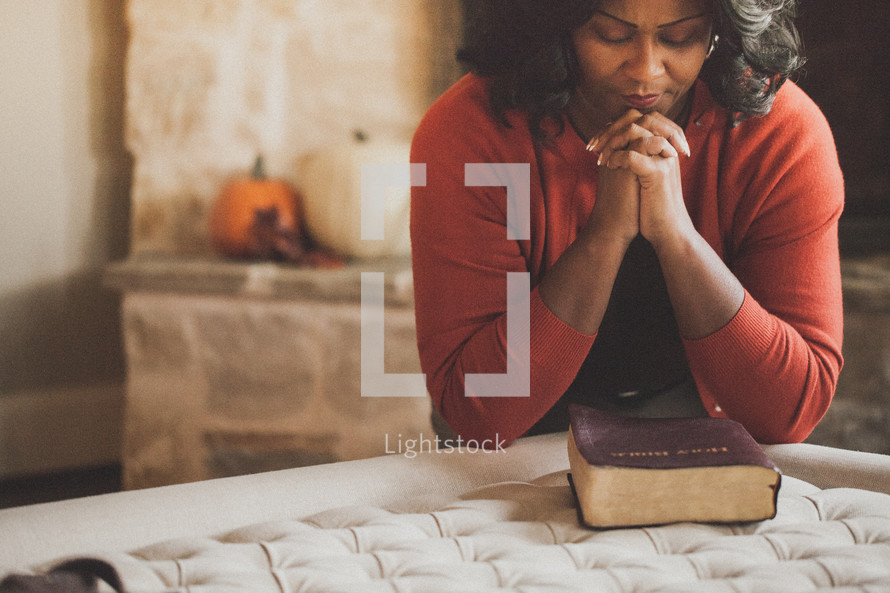 Woman praying over a Bible on the corner of her bed.