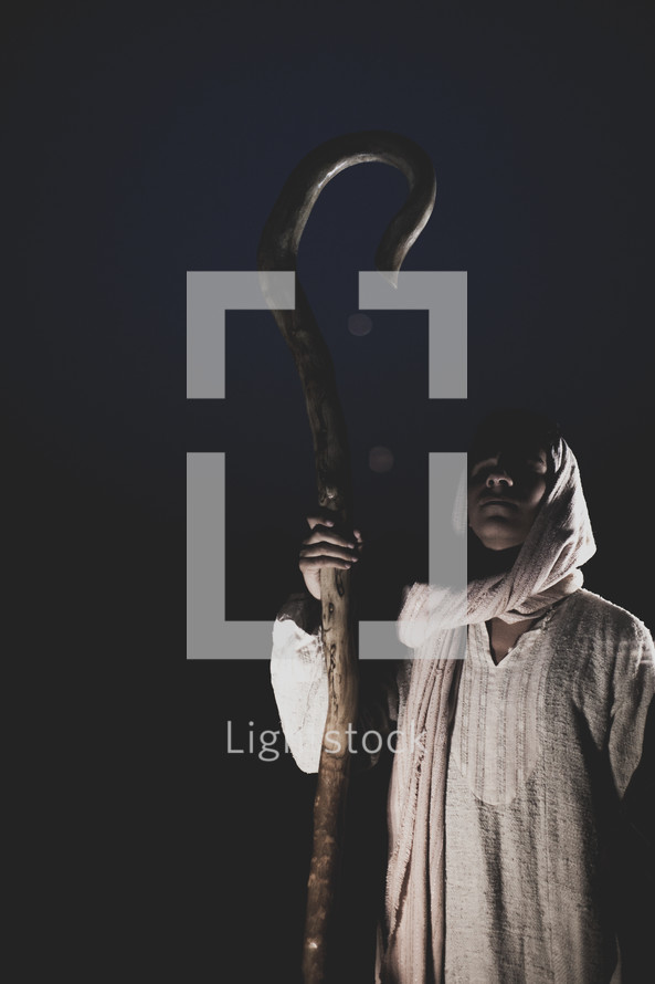 face of a shepherd with his staff standing in darkness 