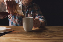 A man pouring coffee from a carafe into a coffee cup.