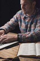 man on a laptop computer with an open  Bible next to him