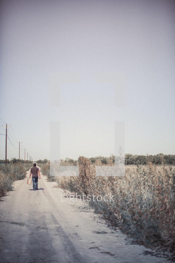 man walking down a dirt road with luggage 
