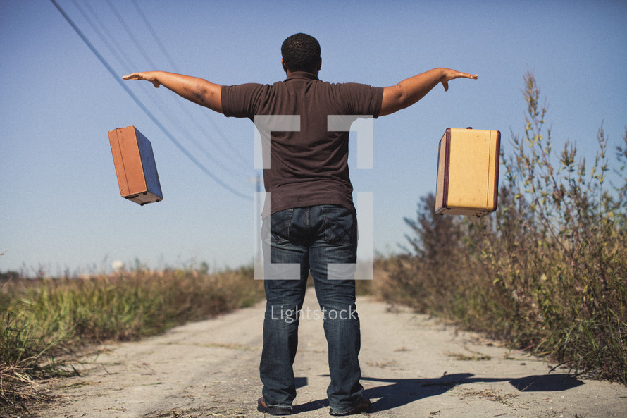 man throwing down luggage on a dirt road 