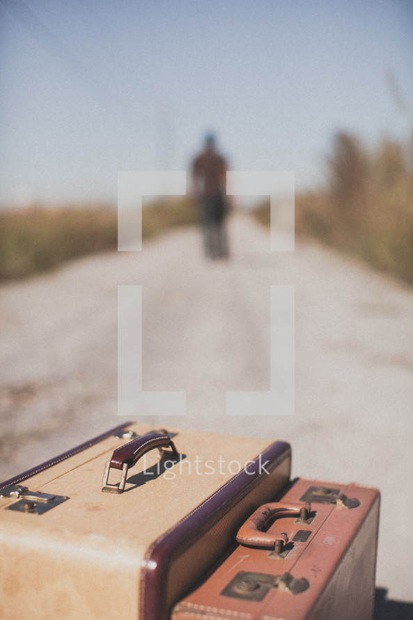 luggage and a man walking away down a dirt road
