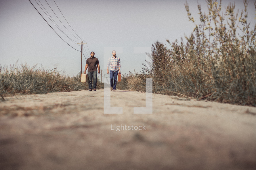 men walking down a dirt road with luggage