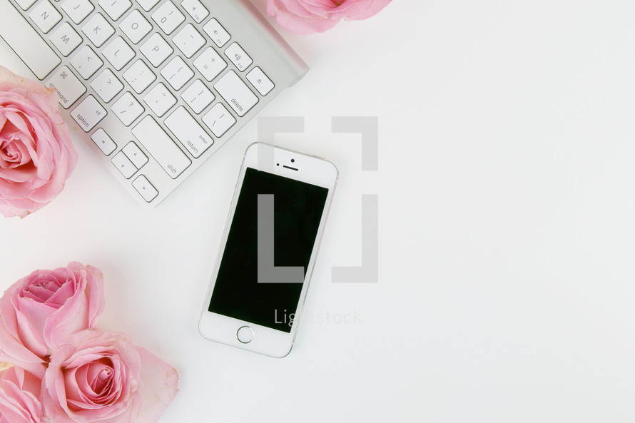 keyboard, pink roses, and cellphone on a white desk 