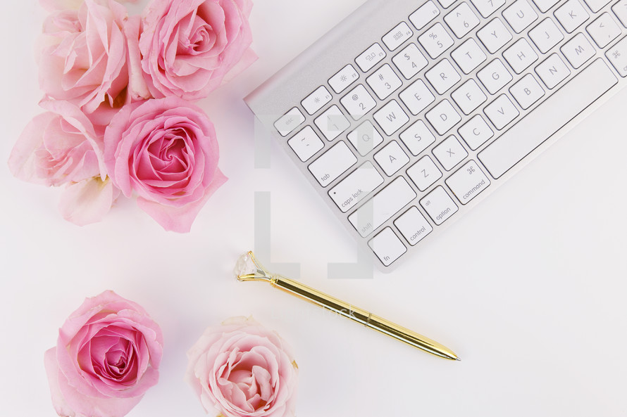 pink roses, gold pen, and keyboard on a white desk 