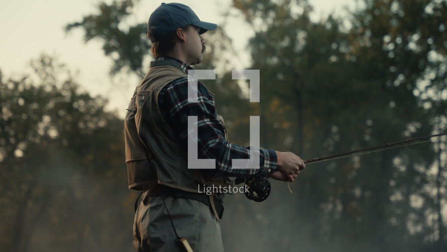 Young fly fisherman casting on a foggy river at sunrise