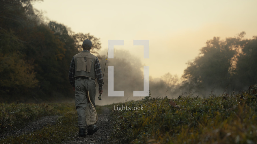 Young fly fisherman walking to a river at dawn