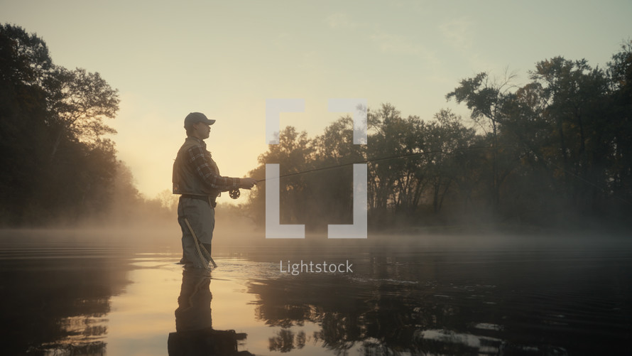 Young fly fisherman casting on a foggy river at sunrise