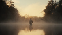 Young fly fisherman casting on a foggy river at sunrise