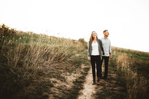 a couple holding hands walking on a dirt road 