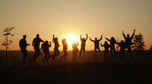 Silhouette of a group of people jumping on the horizon at sunset. 