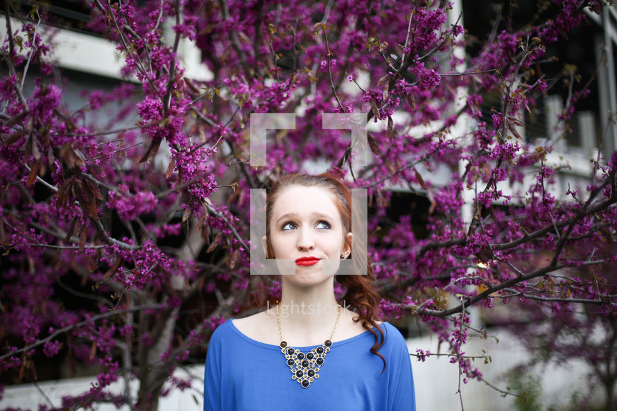 a teen redhead posing for a portrait in front of purple flowers on a tree 