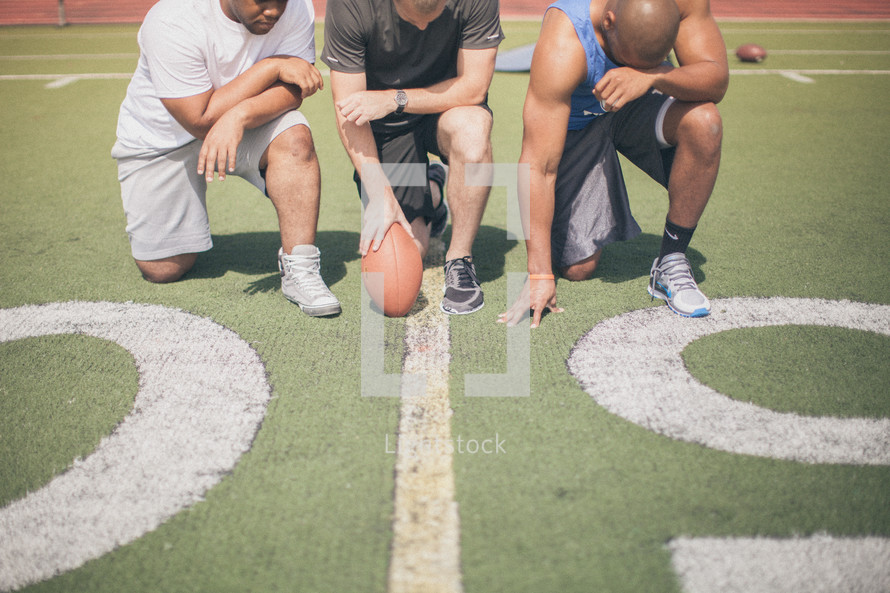 athletes kneeling in prayer on the football field 